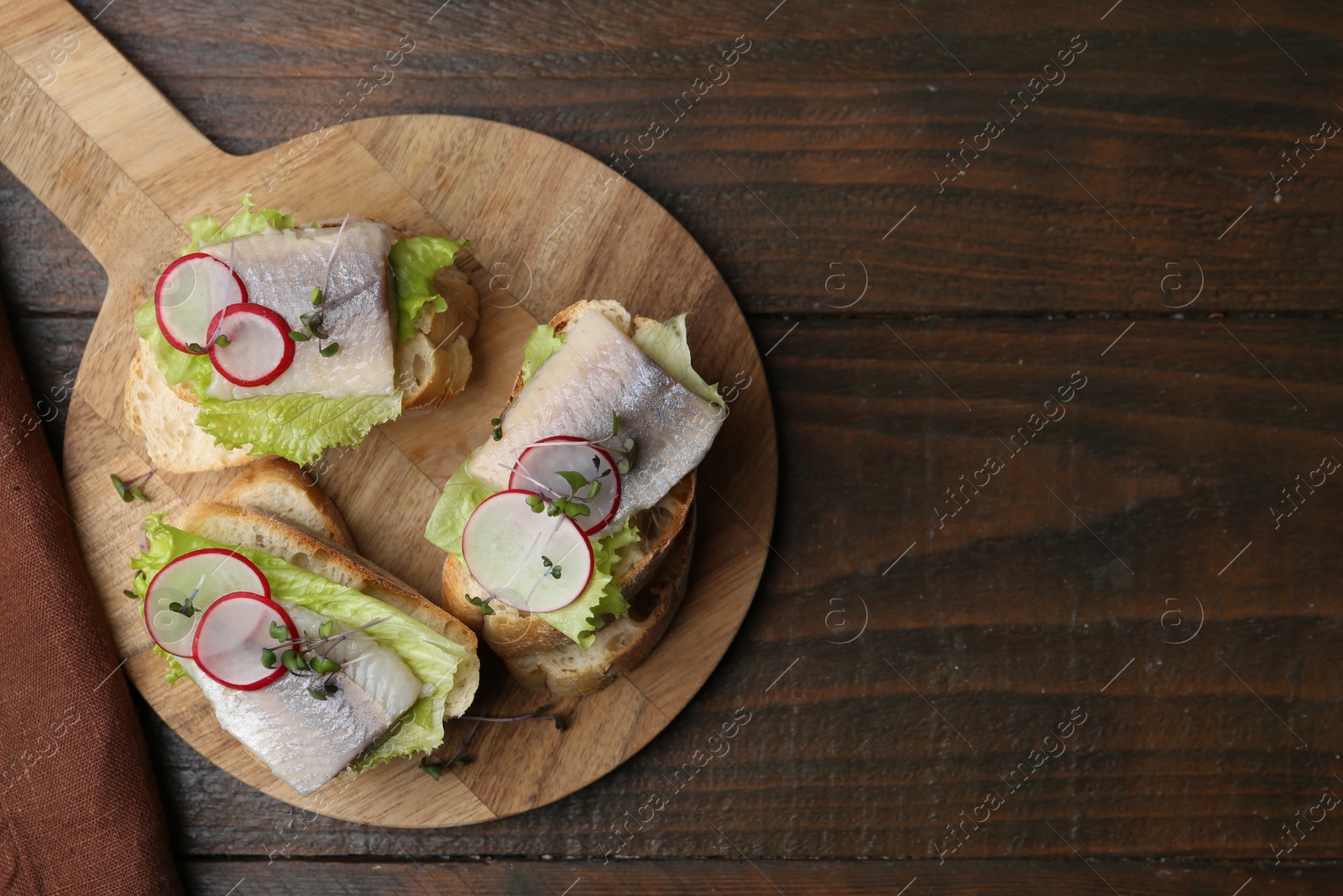 Photo of Tasty sandwiches with herring, radish and lettuce on wooden table, top view. Space for text