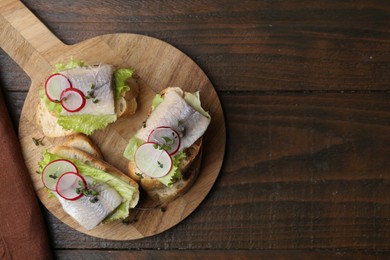 Tasty sandwiches with herring, radish and lettuce on wooden table, top view. Space for text