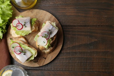 Photo of Tasty sandwiches with herring, radish and lettuce on wooden table, flat lay. Space for text