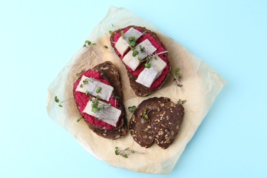 Photo of Tasty sandwiches with herring and horseradish sauce on light blue background, top view