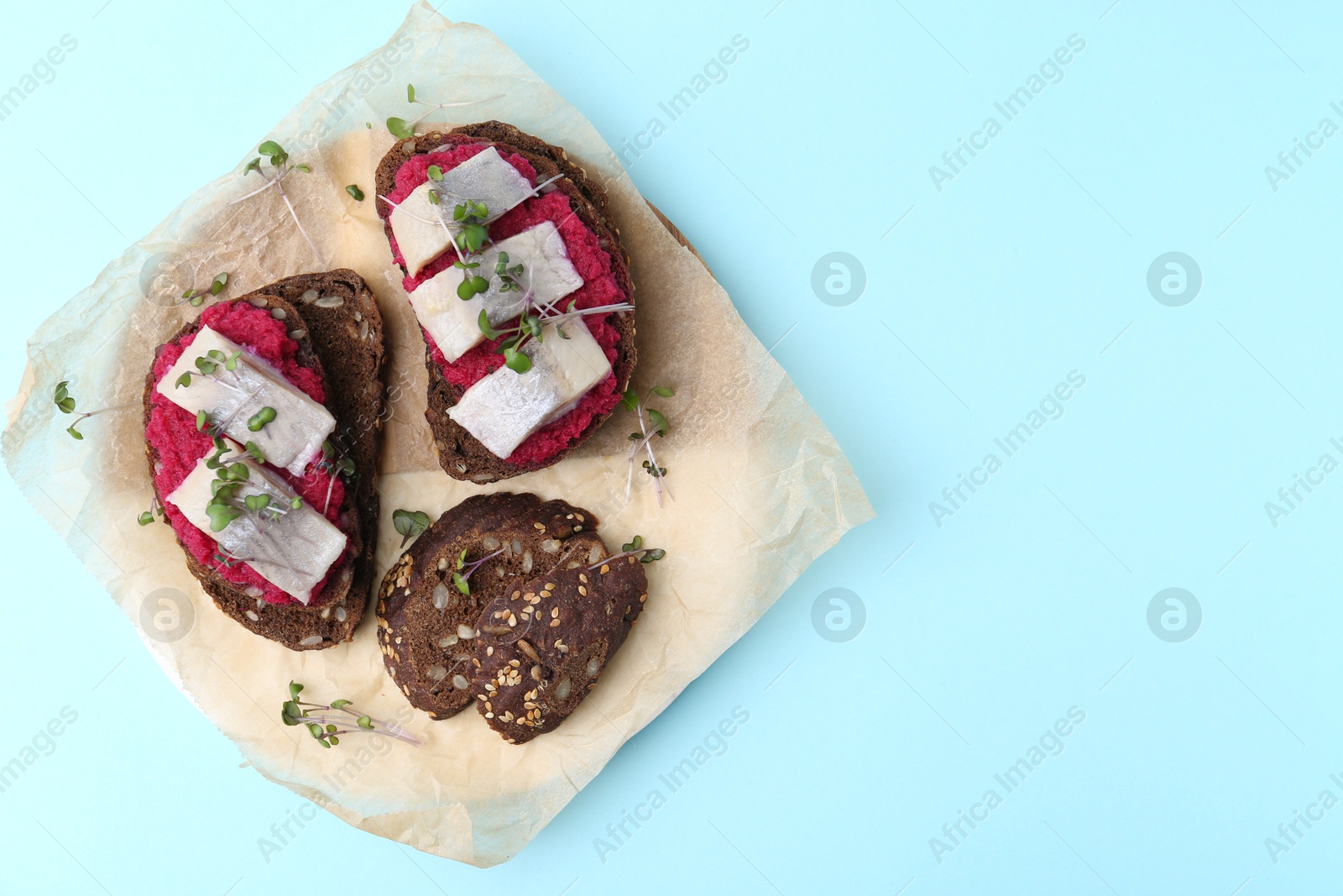 Photo of Tasty sandwiches with herring and horseradish sauce on light blue background, top view. Space for text