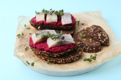 Photo of Tasty sandwiches with herring and horseradish sauce on light blue background, closeup