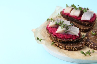 Photo of Tasty sandwiches with herring and horseradish sauce on light blue background, closeup. Space for text