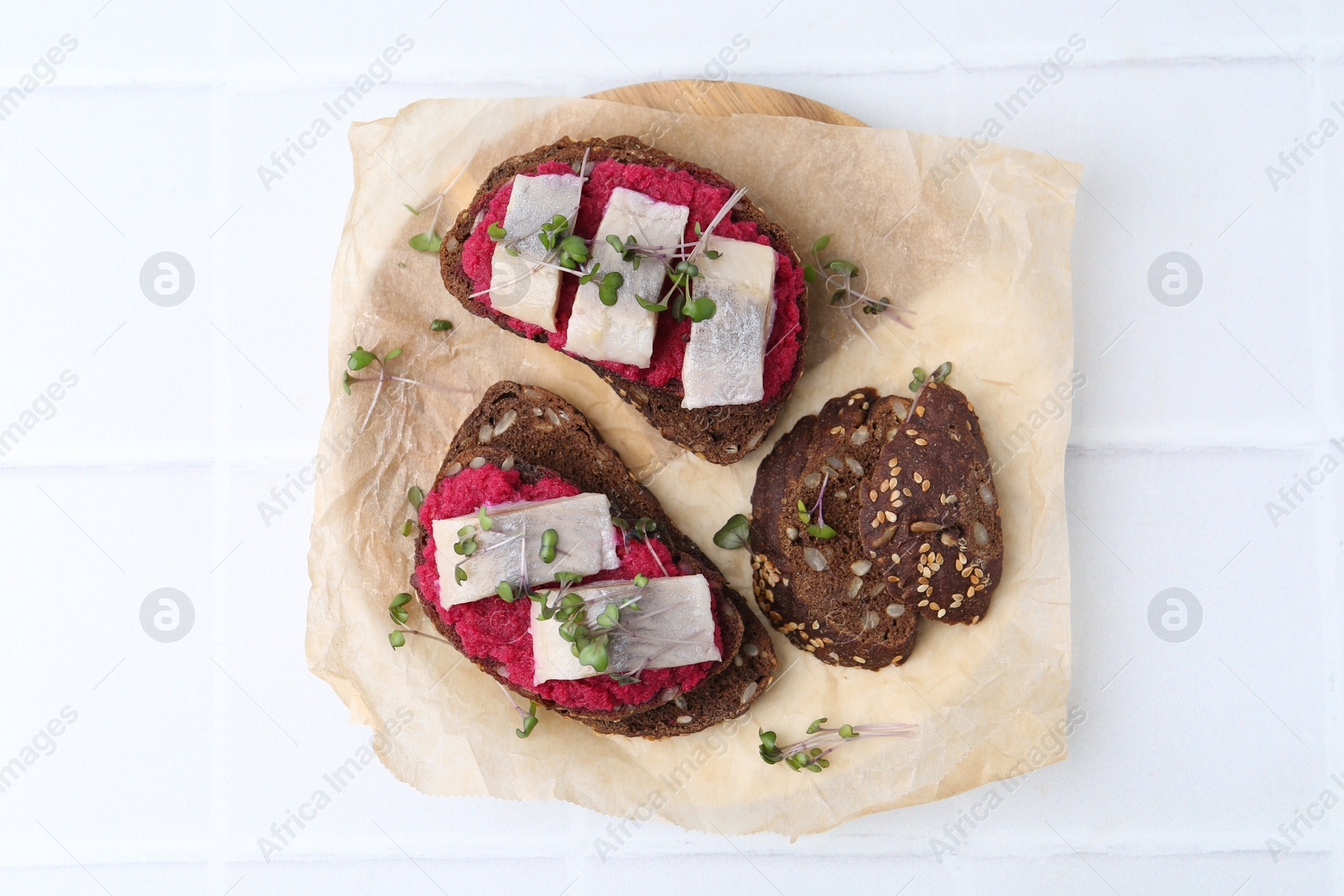 Photo of Tasty sandwiches with herring and horseradish sauce on white tiled table, top view