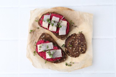 Photo of Tasty sandwiches with herring and horseradish sauce on white tiled table, top view