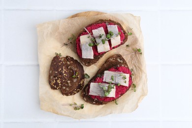 Photo of Tasty sandwiches with herring and horseradish sauce on white tiled table, top view