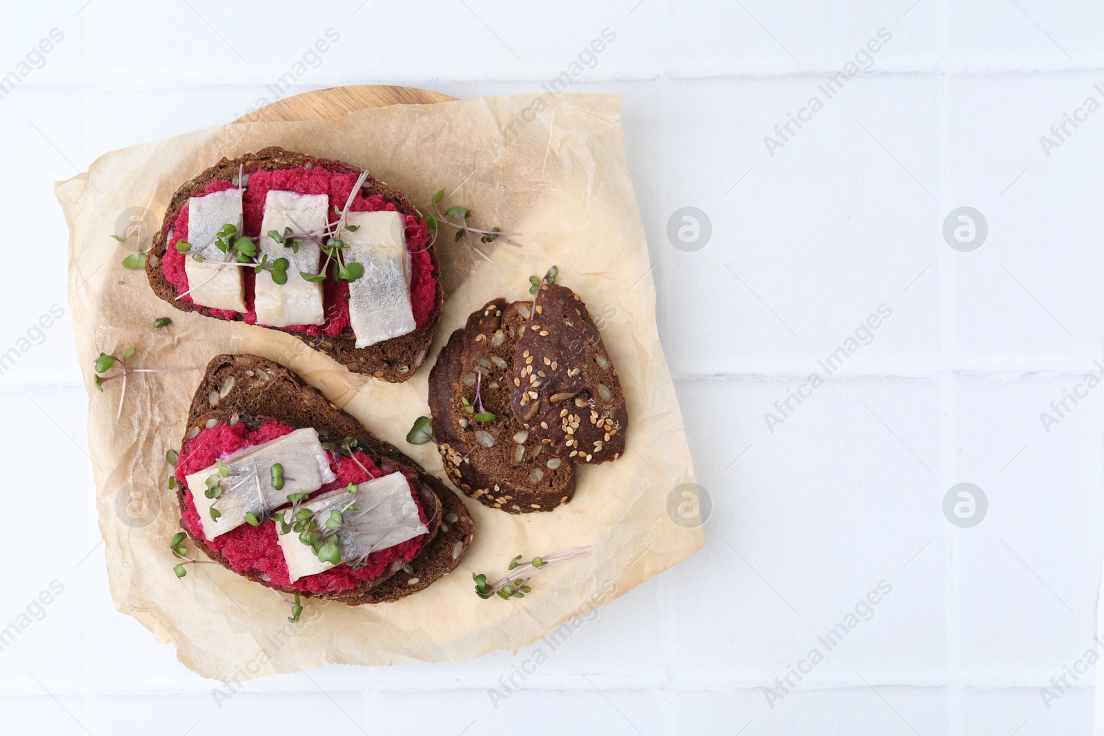 Photo of Tasty sandwiches with herring and horseradish sauce on white tiled table, top view. Space for text