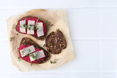 Photo of Tasty sandwiches with herring and horseradish sauce on white tiled table, top view. Space for text