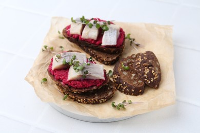 Photo of Tasty sandwiches with herring and horseradish sauce on white tiled table, closeup