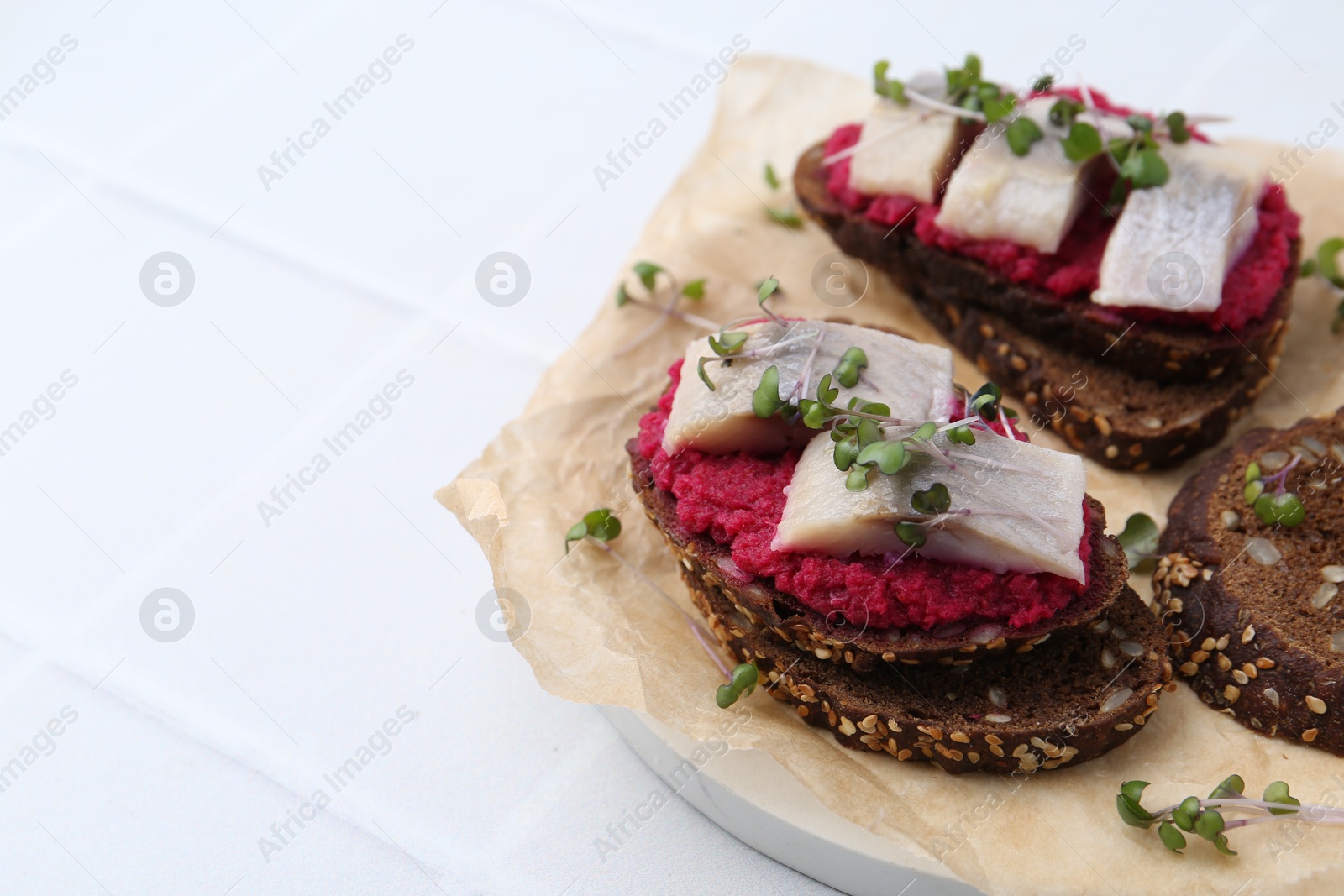 Photo of Tasty sandwiches with herring and horseradish sauce on white tiled table, closeup. Space for text