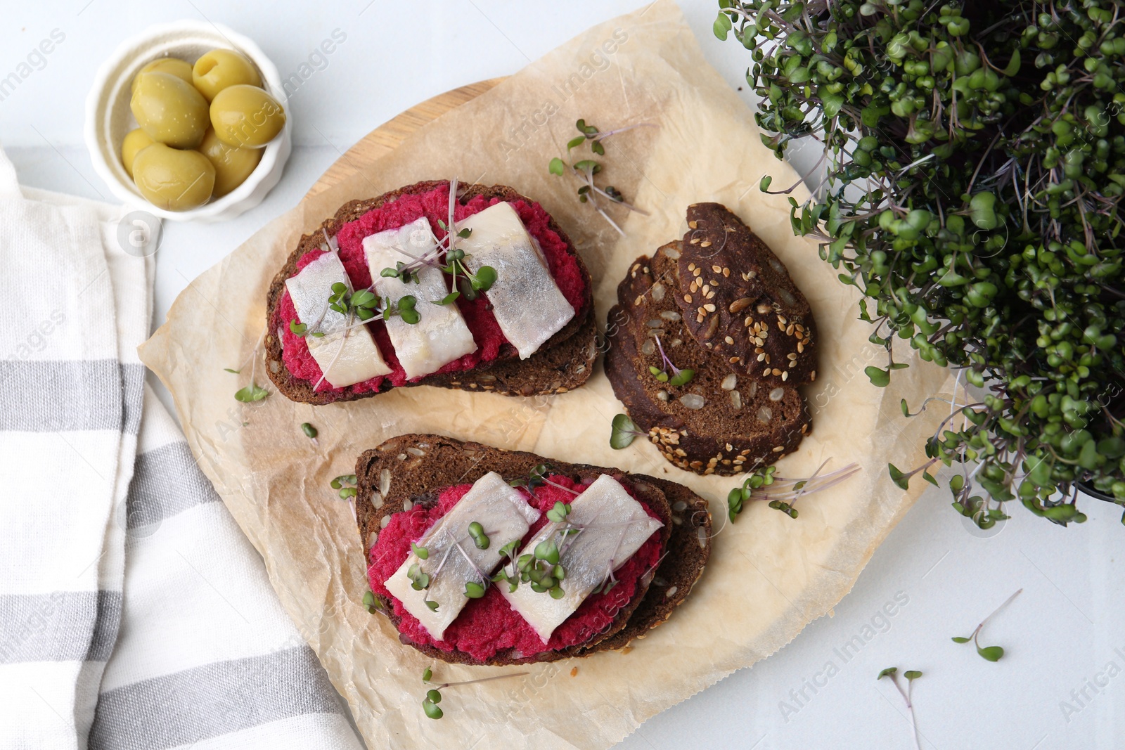 Photo of Tasty sandwiches with herring, horseradish sauce and olives on white table, flat lay