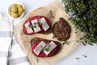 Photo of Tasty sandwiches with herring, horseradish sauce and olives on white table, flat lay