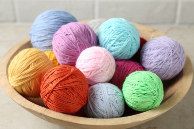 Photo of Balls of colorful yarn in bowl on light grey table, closeup