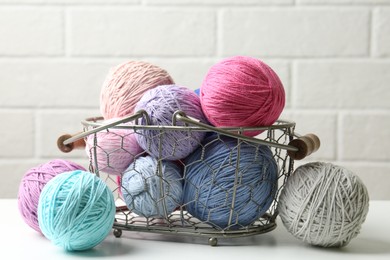 Balls of colorful yarn in metal basket on white wooden table, closeup