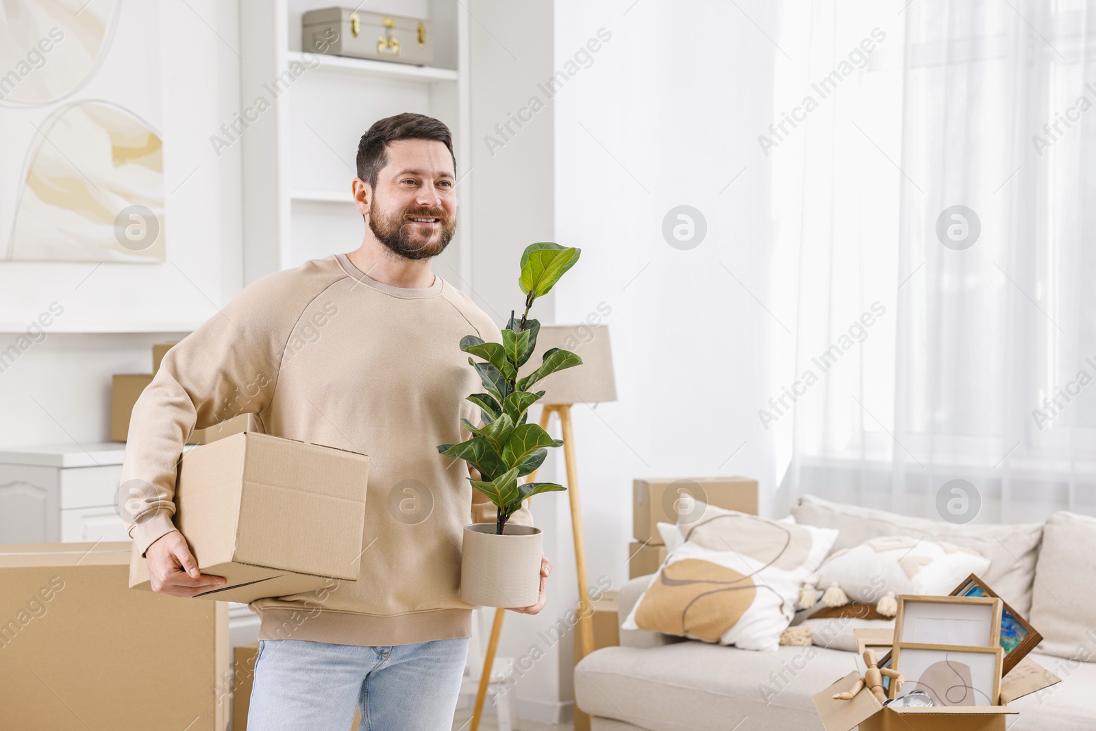 Photo of Moving day. Man with cardboard box and houseplant in his new home