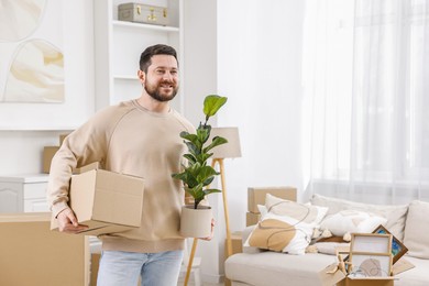 Photo of Moving day. Man with cardboard box and houseplant in his new home