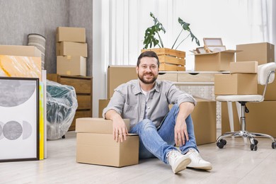 Photo of Moving day. Man resting on floor near cardboard boxes in his new home