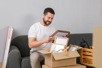 Photo of Moving day. Man unpacking box on sofa in his new home