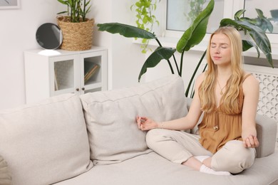 Photo of Feng shui. Young woman meditating on couch at home