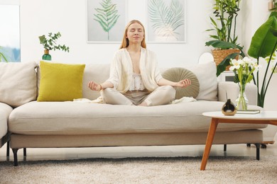 Photo of Feng shui. Young woman meditating on couch at home