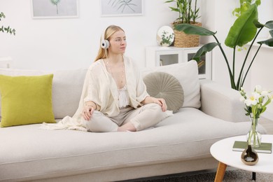 Photo of Feng shui. Young woman with headphones meditating on couch at home