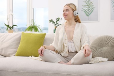 Photo of Feng shui. Young woman with headphones meditating on couch at home