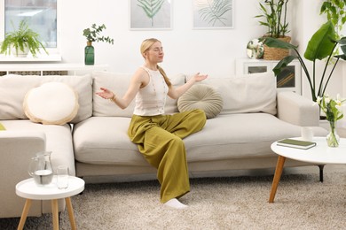 Photo of Feng shui. Young woman meditating on couch at home