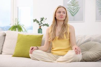 Photo of Feng shui. Young woman meditating on couch at home