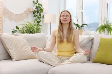 Photo of Feng shui. Young woman meditating on couch at home