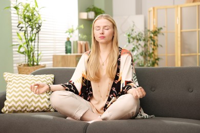 Photo of Feng shui. Young woman meditating on couch at home''