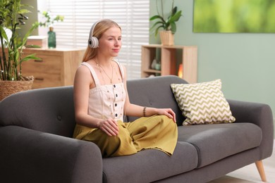 Photo of Feng shui. Young woman with headphones meditating on couch at home''