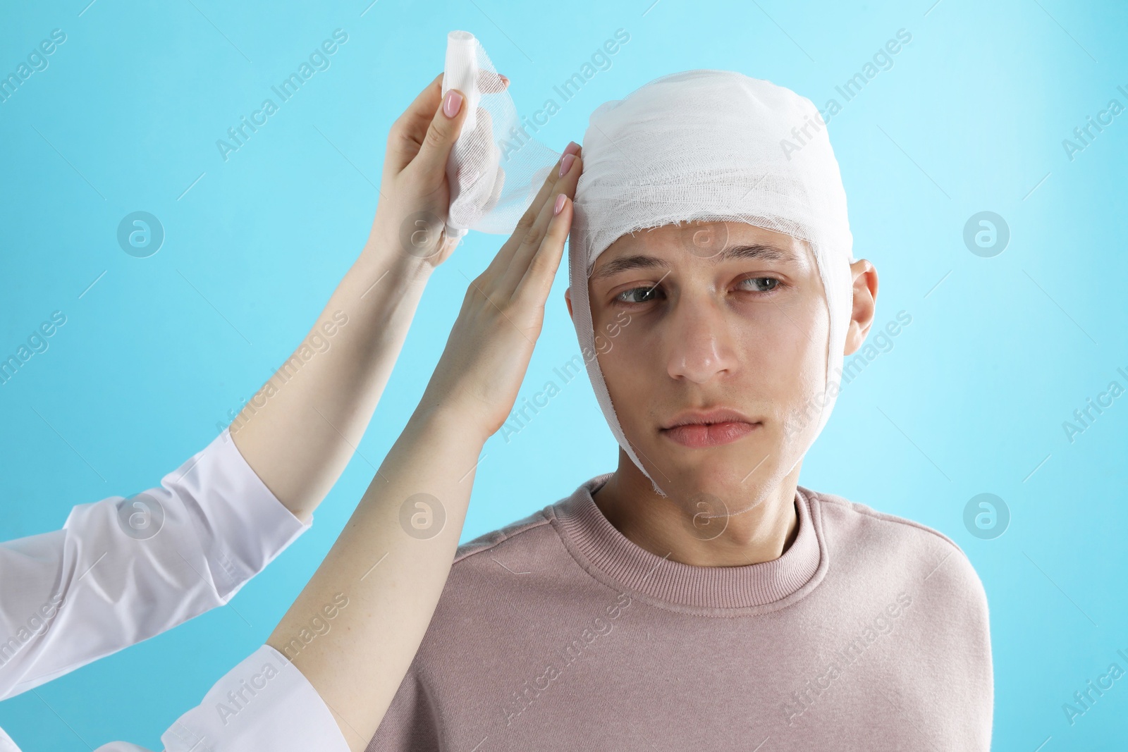 Photo of Doctor bandaging patient's head on light blue background, closeup