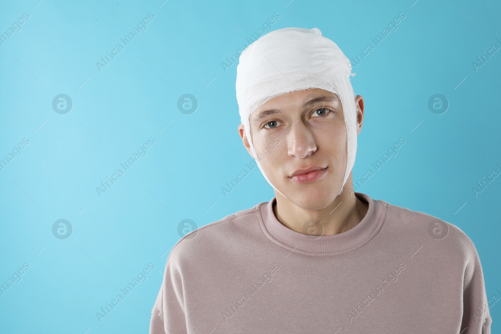 Photo of Man with head wrapped in medical bandage on light blue background, space for text