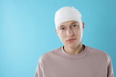 Man with head wrapped in medical bandage on light blue background, space for text