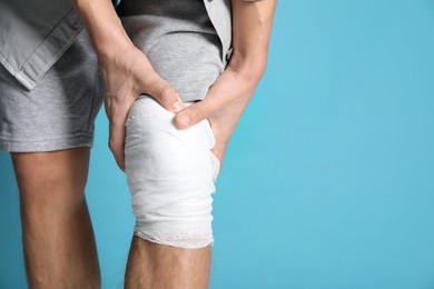 Man with medical bandage on his knee against light blue background, closeup. Space for text