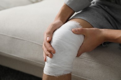 Photo of Man with medical bandage on his knee at home, closeup