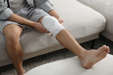 Photo of Man with medical bandage on his knee at home, closeup