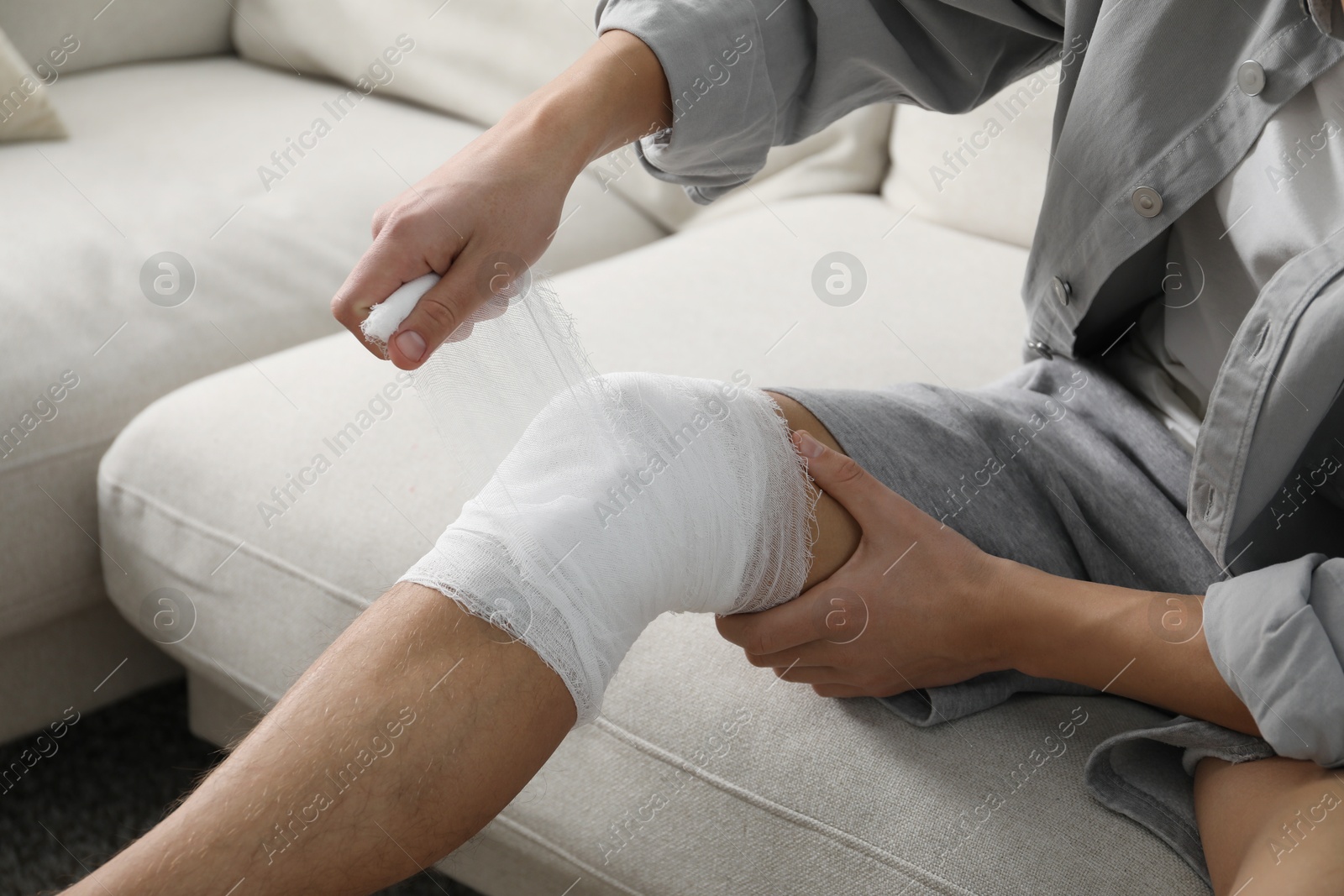 Photo of Man wrapping knee in medical bandage on sofa at home, closeup