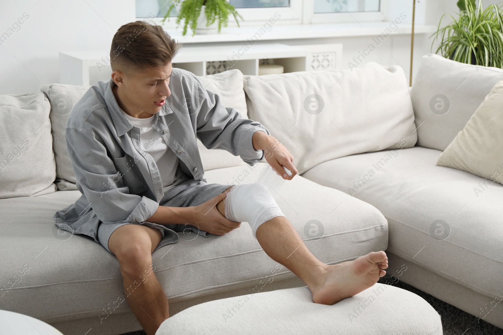 Photo of Man wrapping knee in medical bandage on sofa at home