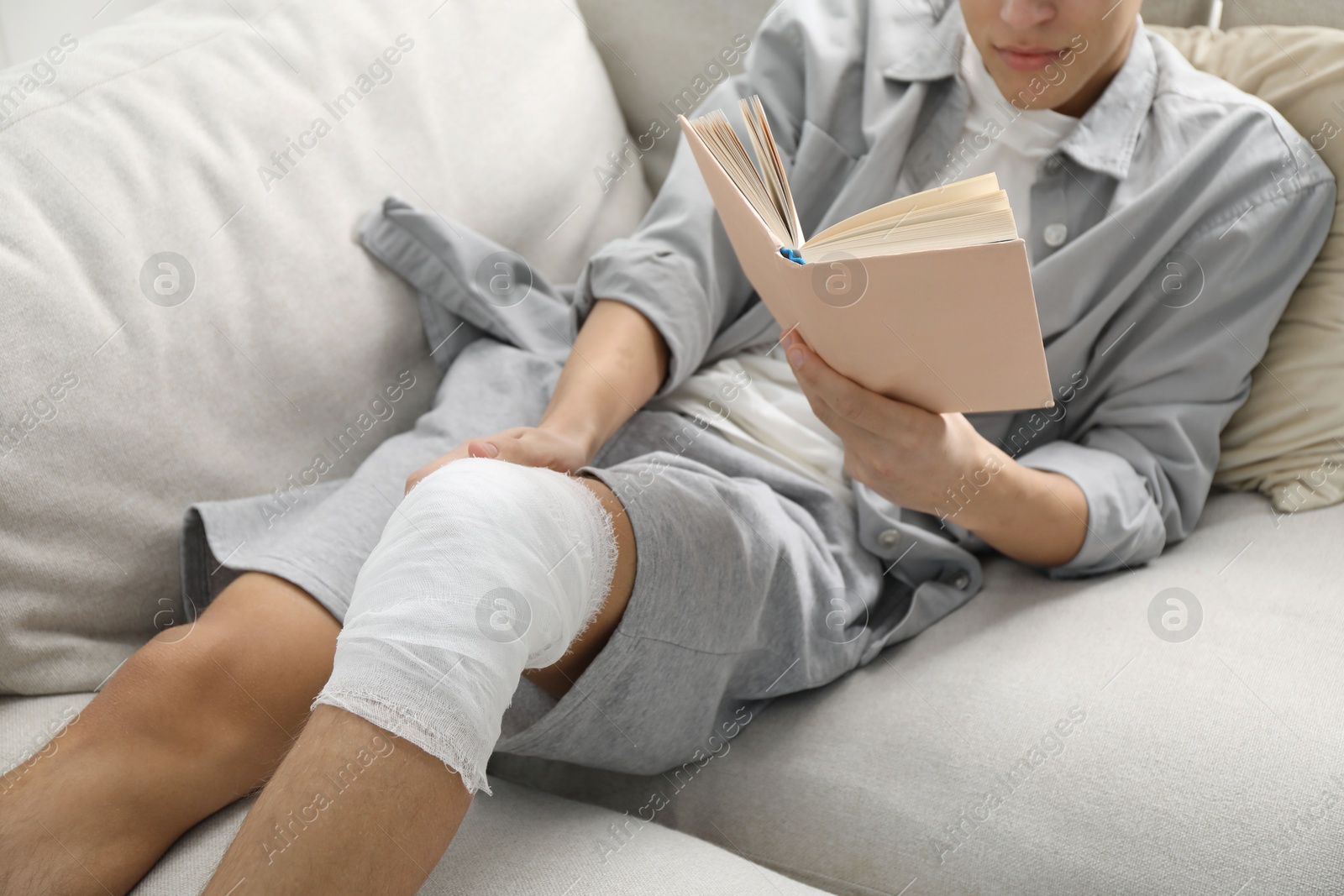 Photo of Man with medical bandage on his knee reading at home, closeup