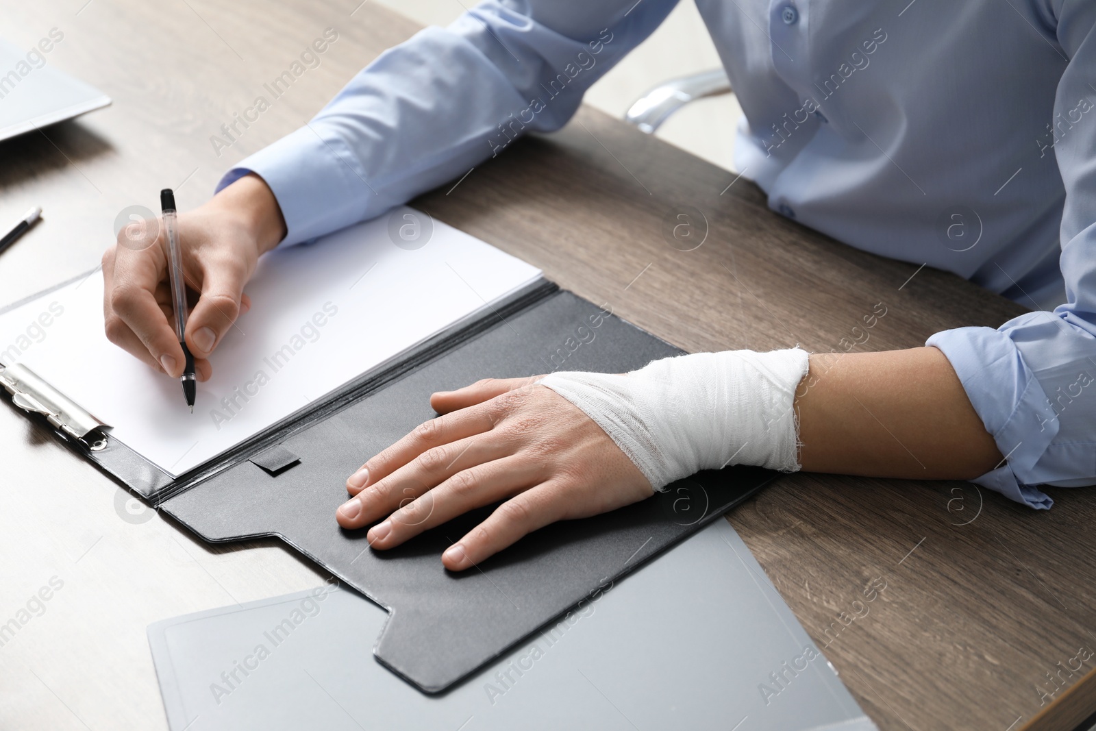 Photo of Man with medical bandage on his wrist working at wooden table indoors, closeup