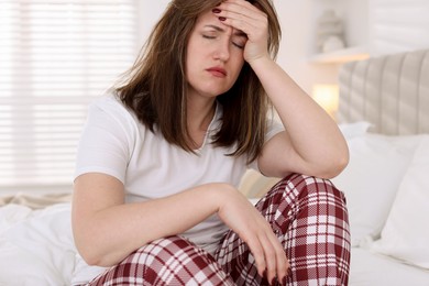 Photo of Unhappy woman suffering from hangover on bed at home