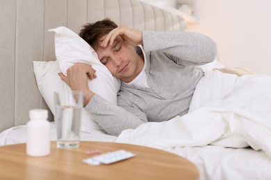 Unhappy young man suffering from hangover on bed at home