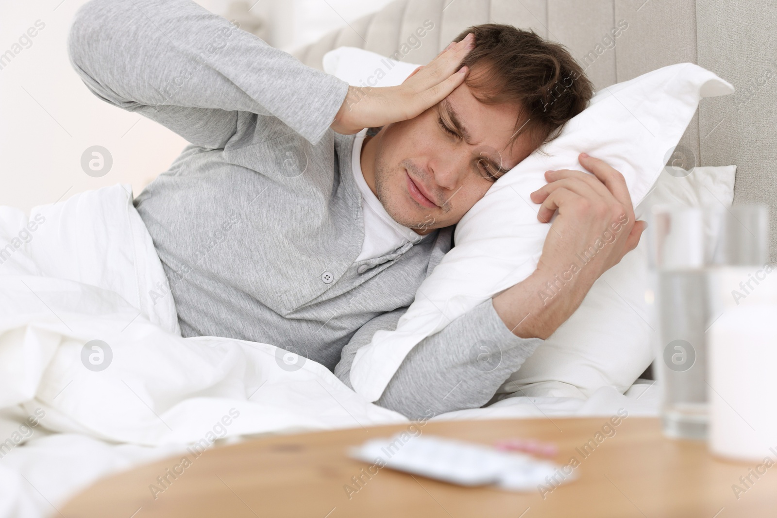 Photo of Unhappy young man suffering from hangover on bed at home