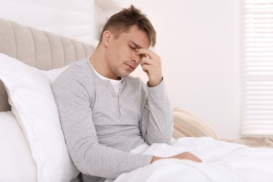 Photo of Unhappy young man suffering from hangover on bed at home, space for text