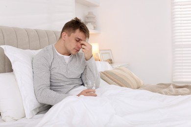 Photo of Unhappy young man with glass of water suffering from hangover on bed at home, space for text