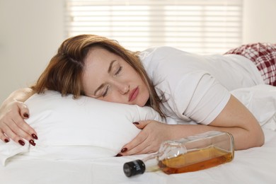 Photo of Suffering from hangover. Woman with bottle of whiskey sleeping on bed at home