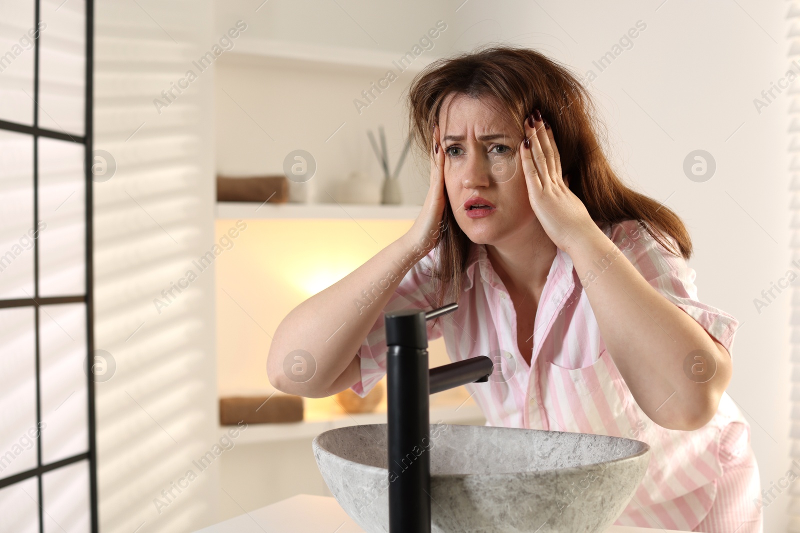 Photo of Unhappy woman suffering from hangover near sink in bathroom