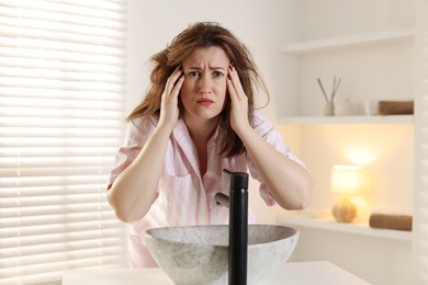 Photo of Unhappy woman suffering from hangover near sink in bathroom