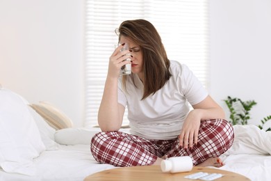 Photo of Unhappy woman with glass of water suffering from hangover on bed at home